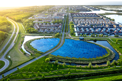 Aerial view of a residential area with a semi-circular solar panel array surrounded by water, greenery, and roads.