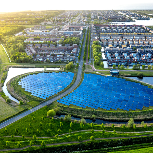 Aerial view of a residential area with a semi-circular solar panel array surrounded by water, greenery, and roads.