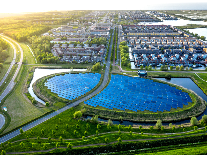 Aerial view of a residential area with a semi-circular solar panel array surrounded by water, greenery, and roads.